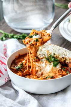 someone is taking a slice of lasagna out of the bowl with their fork