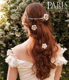 a woman with long red hair wearing a flowered headpiece in front of bushes