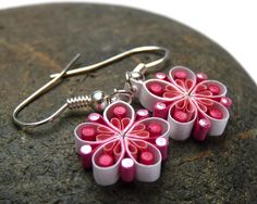 pink and white flower shaped earrings sitting on top of a rock next to a pair of scissors