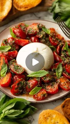 a white plate topped with tomatoes and basil next to bread on top of a table