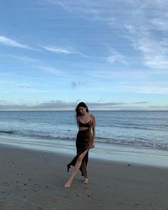 a woman standing on top of a sandy beach next to the ocean with her legs in the air