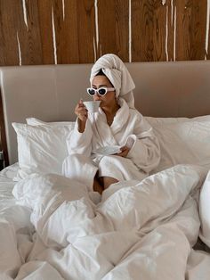 a woman sitting on a bed drinking from a cup