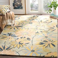 a yellow and blue rug with flowers on the floor in front of a window next to a chair