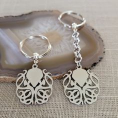 two silver key chains sitting on top of a piece of wood next to a shell