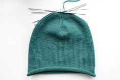 a green knitted hat with two knitting needles on top of it and a pair of scissors next to it