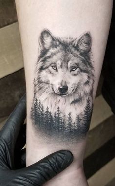 a wolf tattoo on the arm with pine trees and forest in the background, done by person