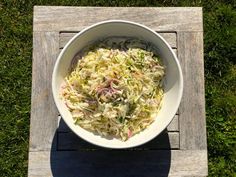 a white bowl filled with coleslaw sitting on top of a wooden table in the grass