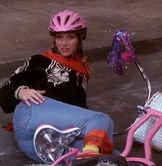 a woman sitting on the ground next to a pink scooter wearing a helmet