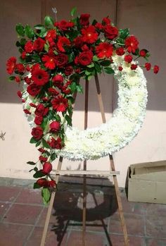 a white wreath with red flowers and greenery on it sitting in front of a building