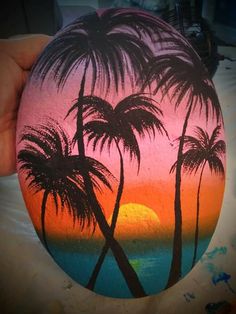 a painted rock with palm trees and the sun setting in the background, on a beach