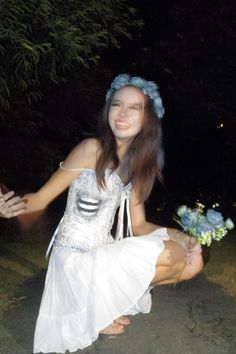 a woman in a white dress is kneeling down with flowers on her head and arm