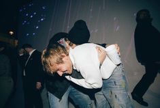 two people hugging each other while standing in front of a wall with lights on it