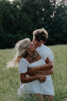 a man and woman hugging in the middle of a field with trees in the background