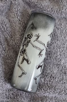 a white and black vase with skeletons on it sitting on a gray carpeted surface