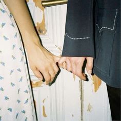 two people holding hands in front of a door with peeling paint on the wall behind them