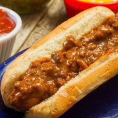 a chili dog on a blue plate next to condiments