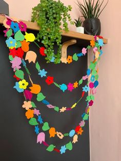 a plant is sitting on a shelf next to a blackboard with colorful paper flowers