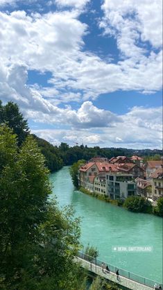 people walking on a bridge over a river with buildings in the background and blue water