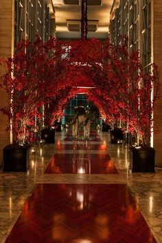 the hallway is decorated with red trees and potted plants in vases on either side