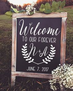 a welcome sign in front of a field with flowers and greenery on the grass