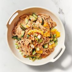 a white bowl filled with pasta and vegetables next to two silver spoons on top of a table