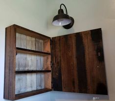 an old wooden cabinet with two shelves and a light on the wall in front of it