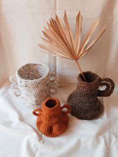 three crocheted vases and a palm leaf on a white cloth covered surface