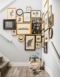 a bunch of framed pictures are hanging on the wall above a stair case with a handbag next to it