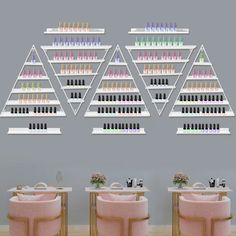 three pink chairs in front of a wall with shelves filled with nail polish bottles on it