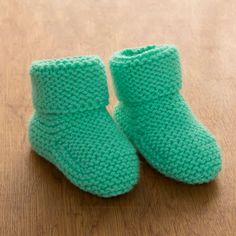 a pair of green knitted baby booties sitting on top of a wooden table