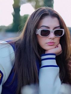 a woman wearing sunglasses leaning on her hand to look at the camera while sitting down