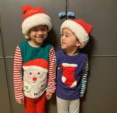 two young children wearing matching christmas pajamas and santa hats, standing next to each other