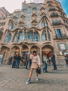 a woman standing in front of a building with lots of windows and people walking around