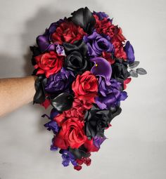 a bridal bouquet with purple, red and black flowers is being held by someone's hand