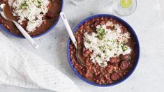 two bowls filled with beans and rice on top of a white table next to a glass of wine