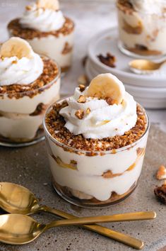 three desserts with banana slices and whipped cream in them on a table next to gold spoons