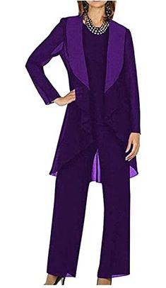 a woman wearing a purple suit and matching pants with a beaded necklace, standing in front of a white background