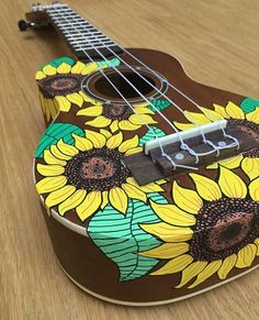 an ukulele with sunflowers painted on it sitting on a wooden table