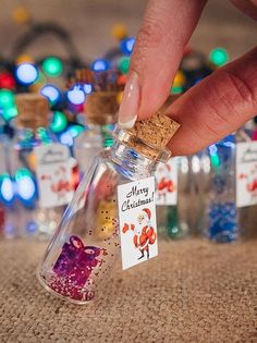 a hand is holding a tiny bottle filled with colorful confetti in front of christmas lights