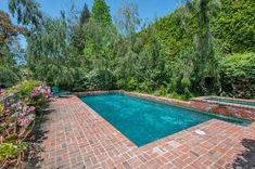 an empty swimming pool surrounded by greenery and brick pavers walkways in the backyard