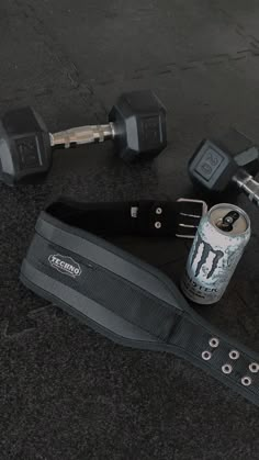 a can of beer and some dumbs are on the ground next to a pair of exercise equipment