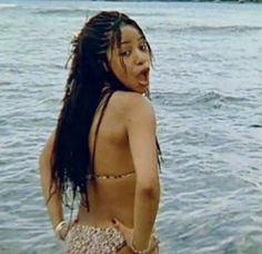 a woman standing in the water with her hair blowing back and wearing a bathing suit