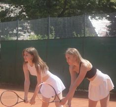 two young women holding tennis racquets on a court