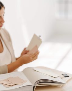 a woman sitting at a table with an open book in front of her and papers on the desk