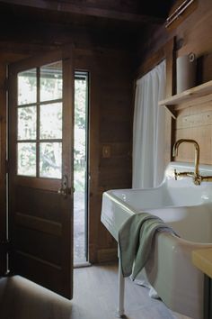 a white sink sitting under a window next to a wooden door in a room with wood paneling