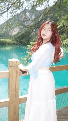 a woman with red hair is standing on a deck near the water and looking off into the distance