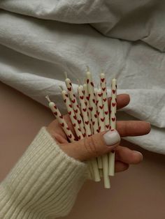 a hand holding several white and red sticks with hearts on them, in front of a blanket