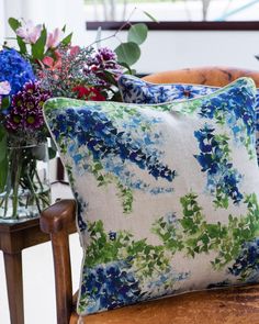 two blue and green floral pillows sitting on a chair next to vases with flowers