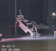 two people standing in front of a car that has been flipped over on its side