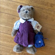 a brown teddy bear wearing a purple dress and holding a blue bag on a wooden floor